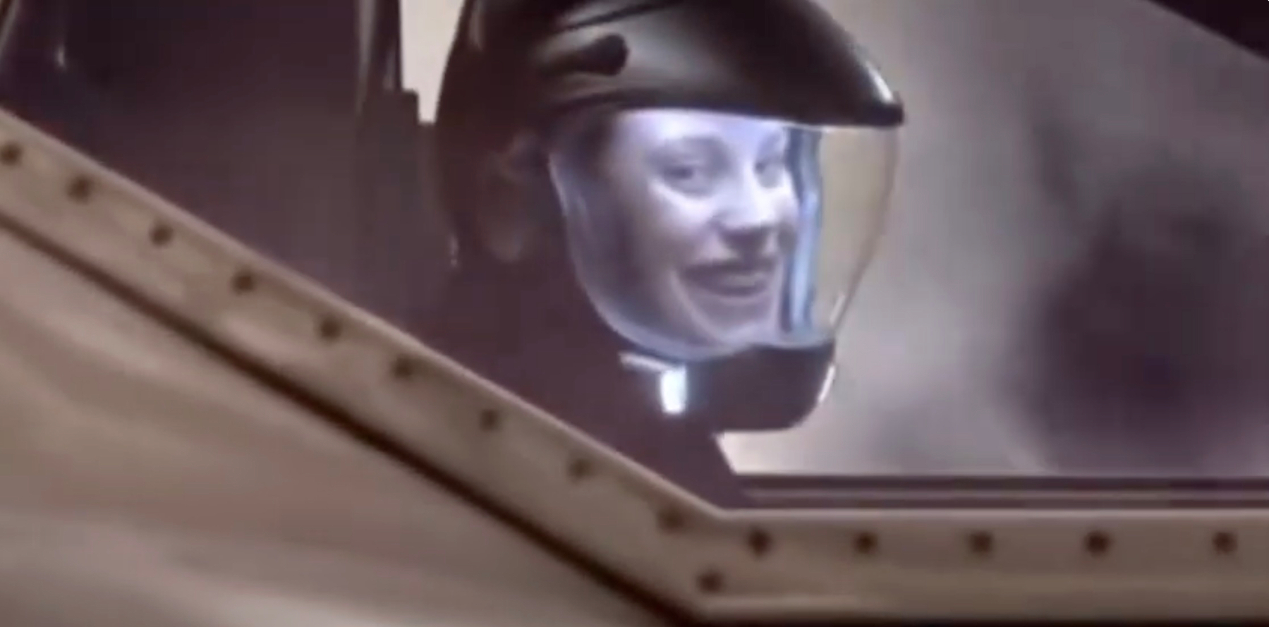 A person wearing a helmet with a transparent visor is inside a vehicle or cockpit. It is Katee Sackhoff playing Starbuck on Battlestar Galactica